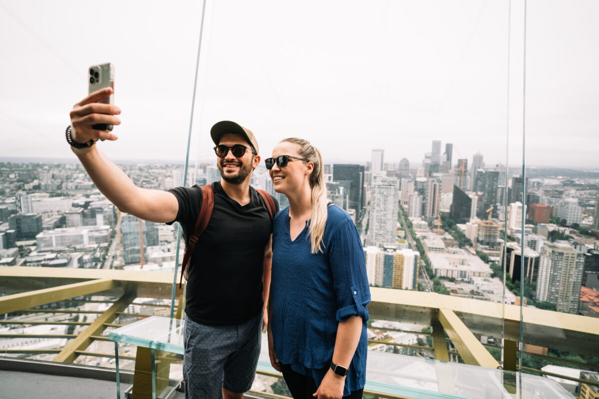 Man and woman taking selfie from the top of the Space Needle with city skyline in the back.