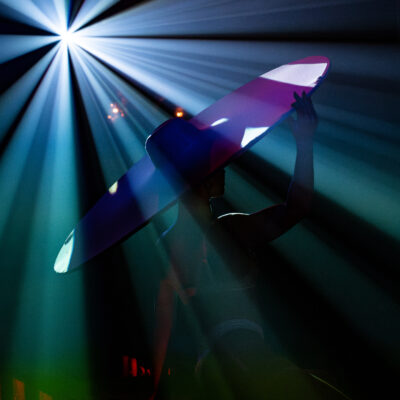 Can Can Culinary Cabaret woman in large hat with stage lights in the background.