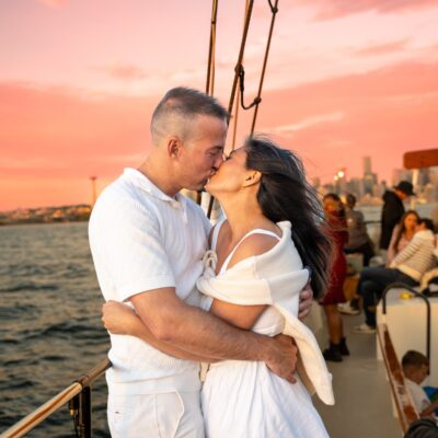 Couple embrace on ship with Seattle sunset.